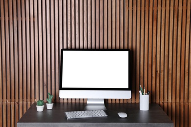 Modern computer monitor on desk against wooden wall, mock up with space for text