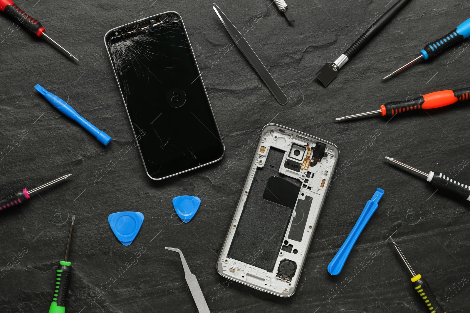 Photo of Damaged smartphone and repair tools on black background, flat lay