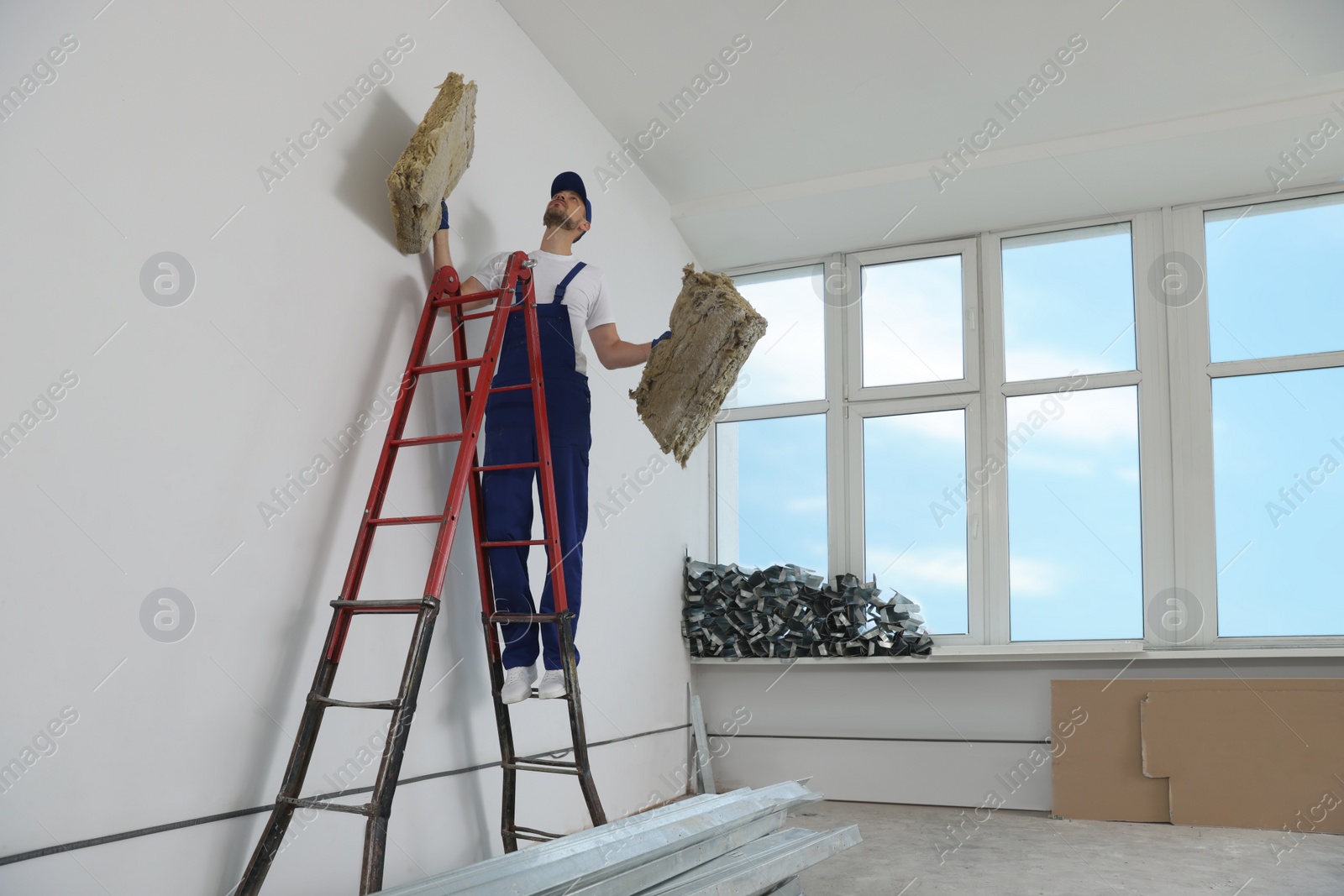 Photo of Construction worker with used glass wool on stepladder in room prepared for renovation