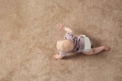 Photo of Cute little baby crawling on carpet indoors, top view with space for text