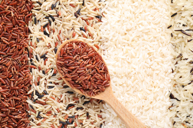 Photo of Different types of rice with wooden spoon, top view