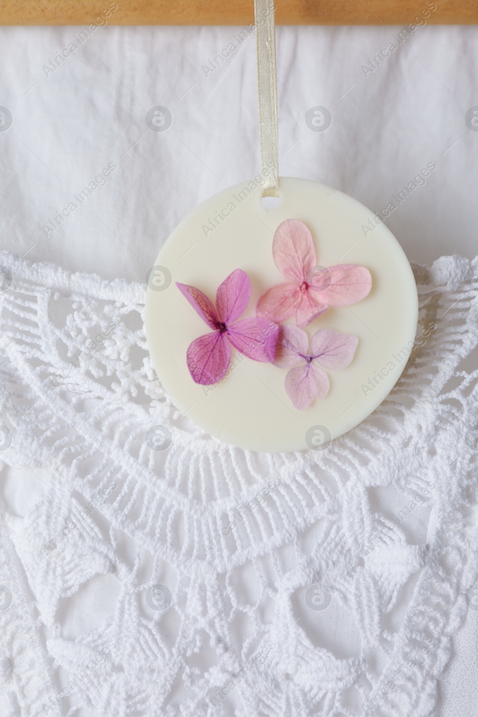 Photo of Scented sachet with flowers hanging near stylish clothes, closeup view