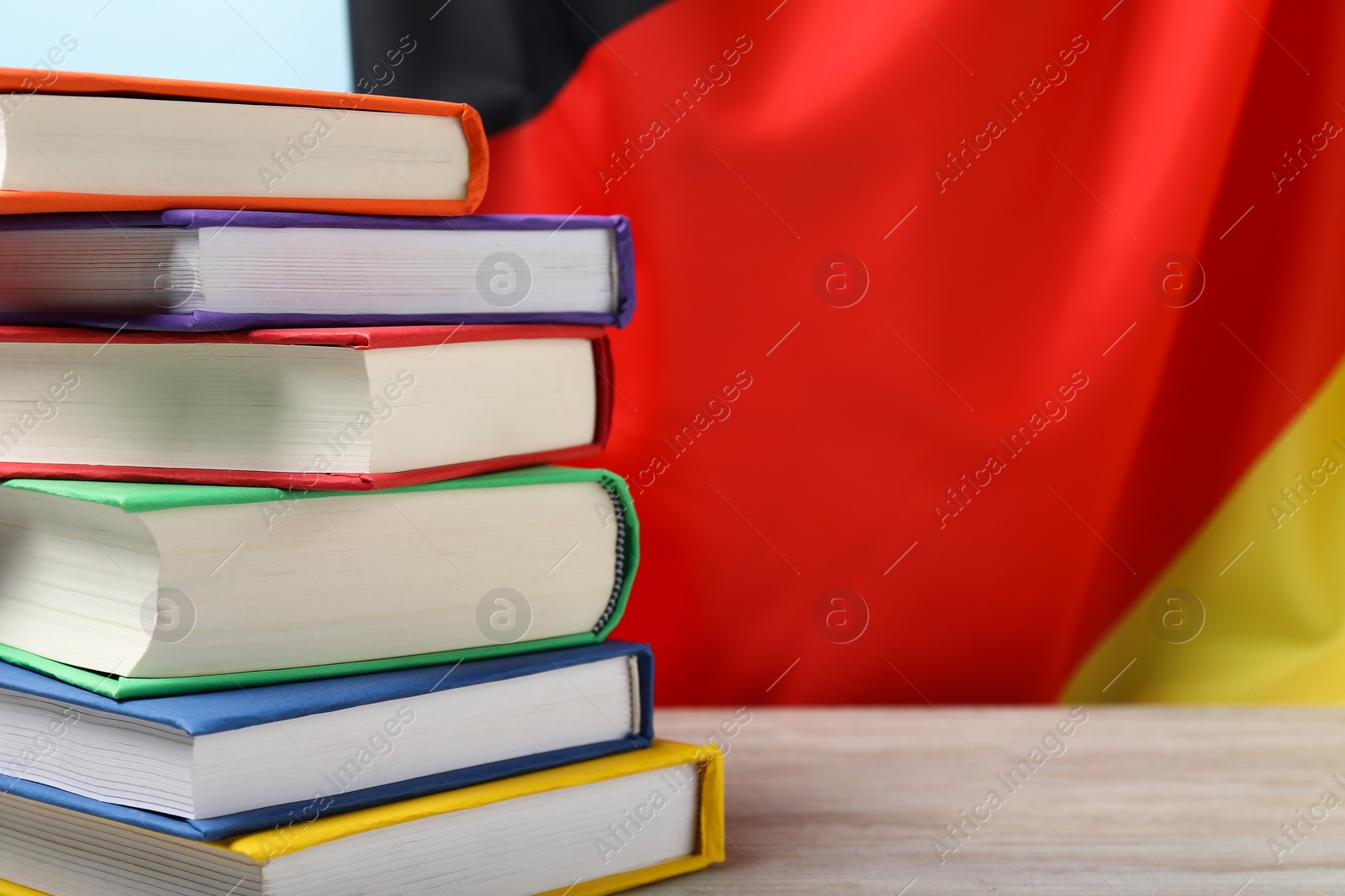 Photo of Learning foreign language. Different books on wooden table near flag of Germany, space for text