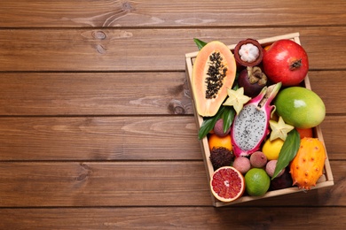 Crate with different exotic fruits on wooden table, top view. Space for text