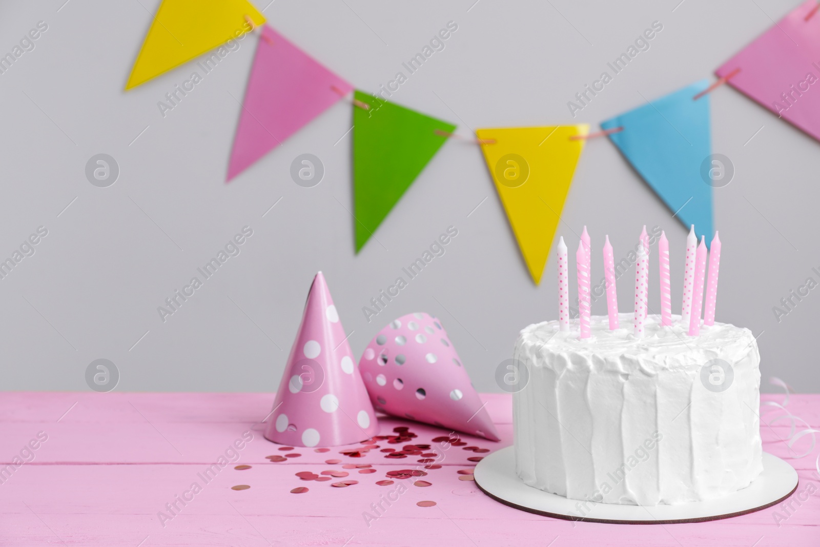 Photo of Delicious cake with candles and party hats on pink wooden table. Space for text