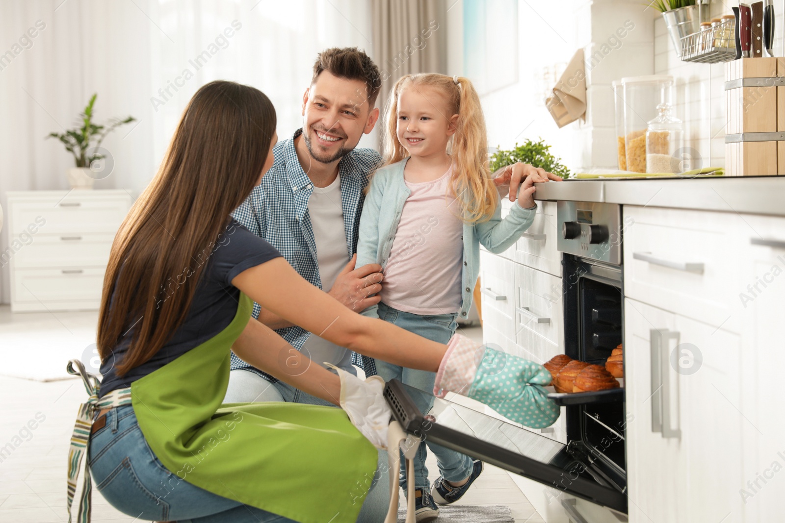 Photo of Woman and her family taking out tray with baked buns from oven in kitchen