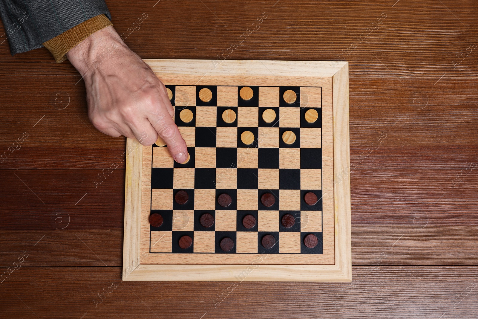 Photo of Playing checkers. Senior man thinking about next move at wooden table, top view