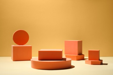 Photo of Many orange geometric figures on table against yellow background, space for text. Stylish presentation for product