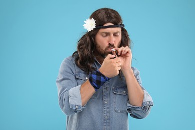 Photo of Stylish hippie man lighting cigarette on light blue background