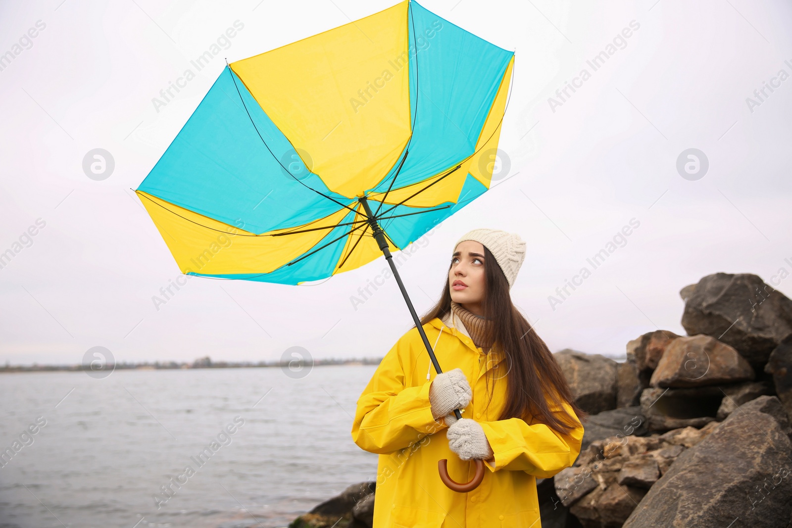Photo of Woman in yellow raincoat with umbrella caught in gust of wind near river