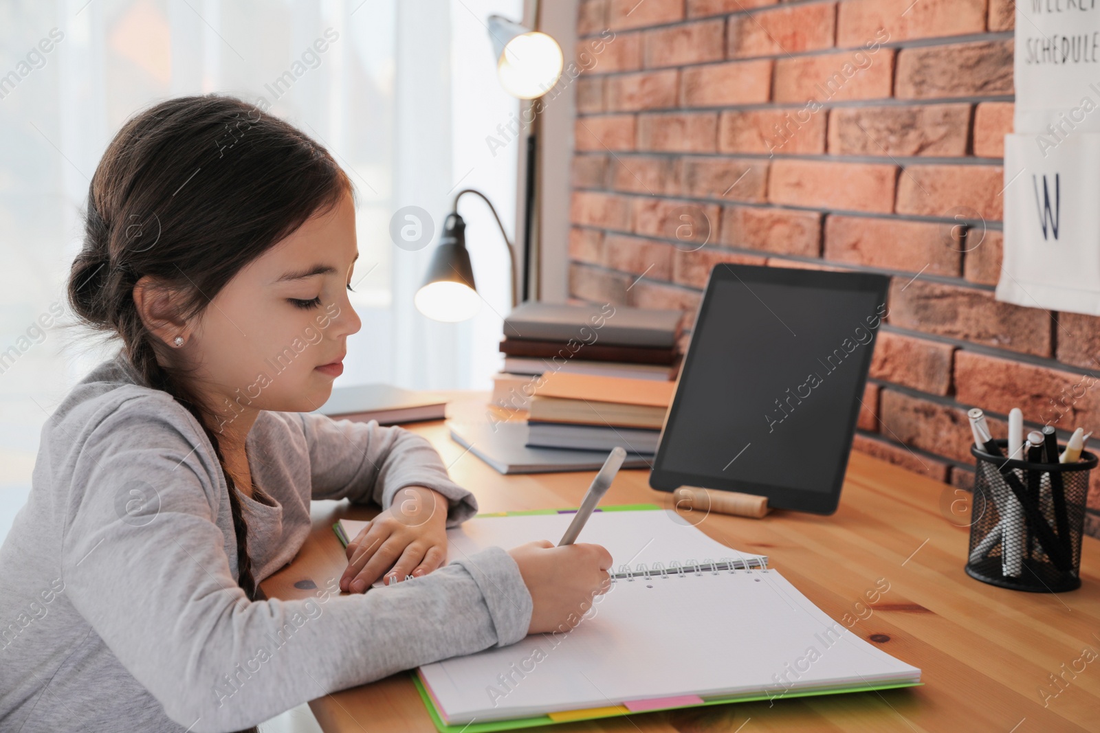 Photo of Little girl doing homework with modern tablet at home