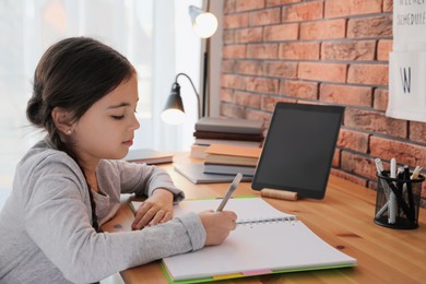 Little girl doing homework with modern tablet at home