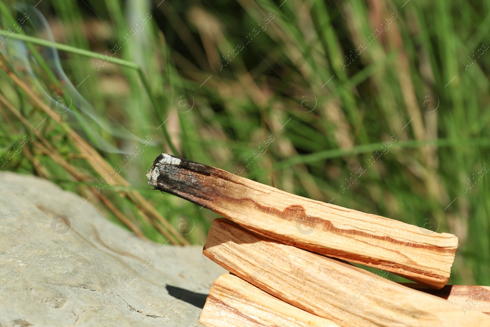 Photo of Smoldering palo santo sticks on stone outdoors, closeup. Space for text