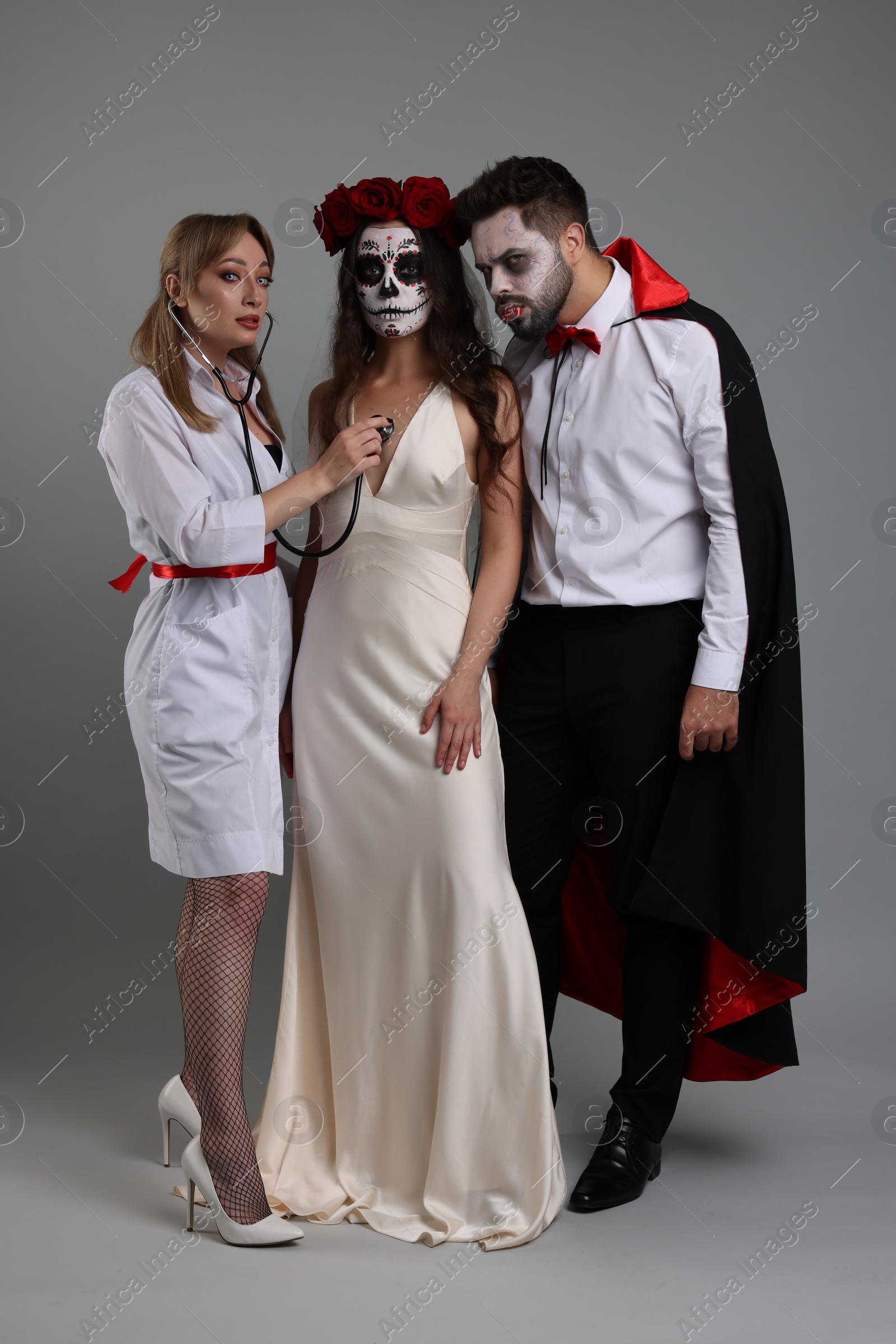 Photo of Group of people in scary costumes on light grey background. Halloween celebration