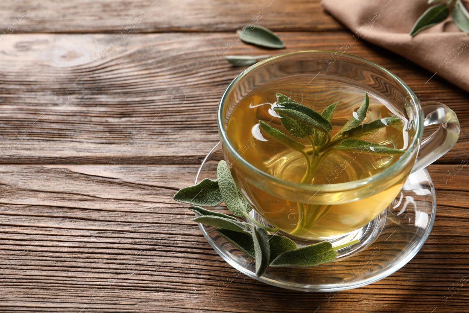 Photo of Cup of aromatic sage tea and fresh leaves on wooden table. Space for text