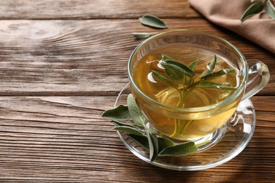 Photo of Cup of aromatic sage tea and fresh leaves on wooden table. Space for text