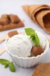 Scoops of tasty ice cream with mint leaves and caramel candies on white table, closeup