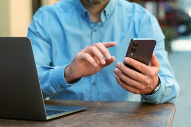 Man using smartphone at table in outdoor cafe, closeup
