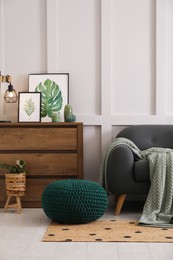 Photo of Stylish living room interior with knitted pouf, sofa and wooden chest of drawers