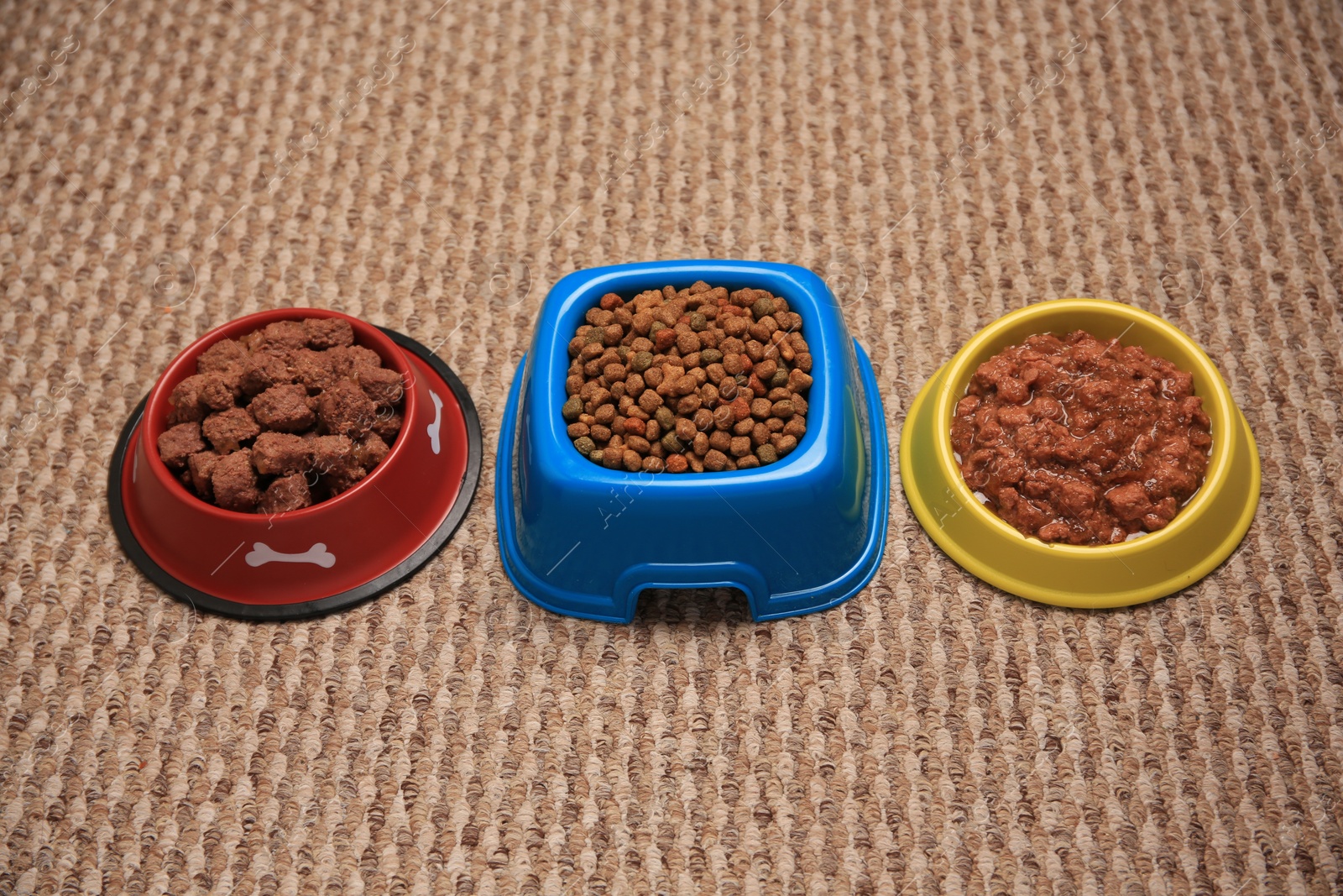 Photo of Dry and wet pet food in feeding bowls on soft carpet, above view