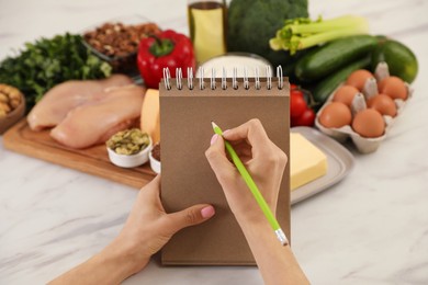 Woman writing in notebook near products at table, closeup. Keto diet