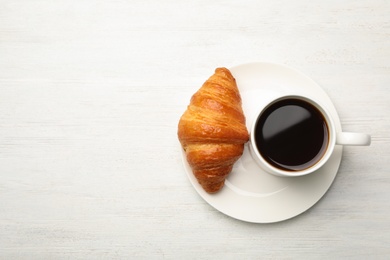 Photo of Plate with cup of coffee and croissant on white wooden background, flat lay. Space for text