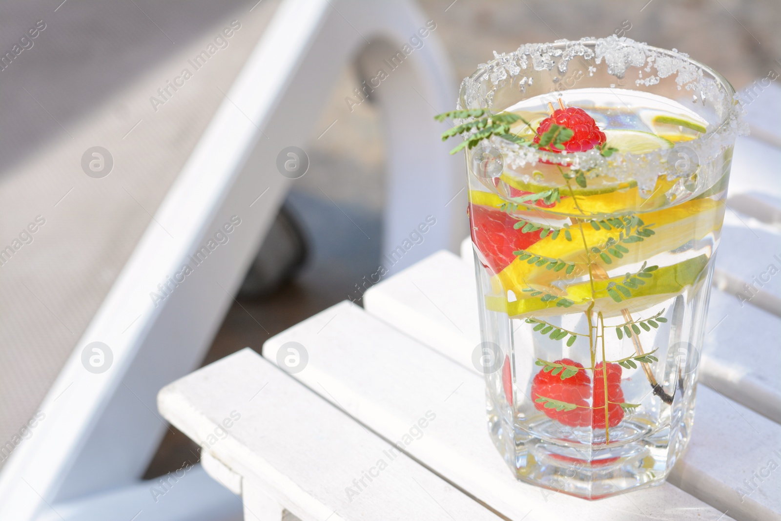 Photo of Delicious refreshing lemonade with raspberries on white wooden table outdoors, closeup. Space for text