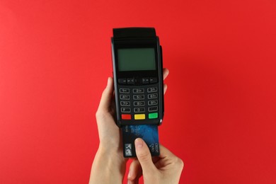 Woman with credit card using modern payment terminal on red background, closeup