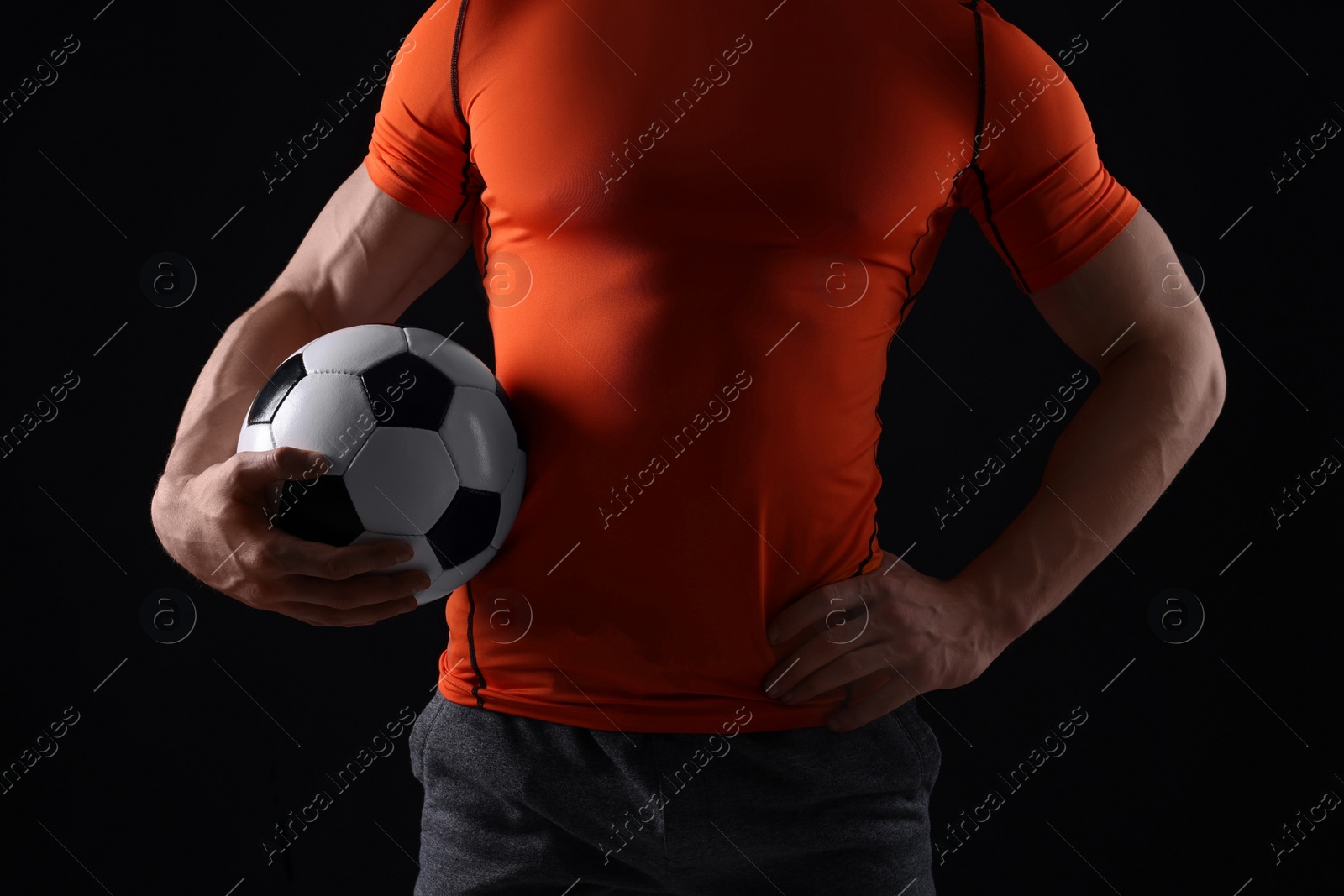 Photo of Athletic man with soccer ball on black background, closeup