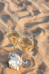 Glasses of tasty wine and seashell on sand, space for text