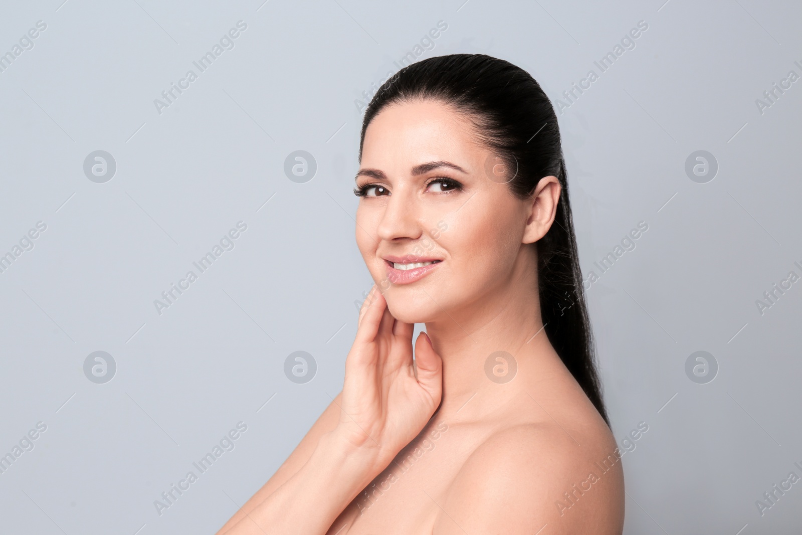 Photo of Beautiful woman with clean skin touching her face on light background