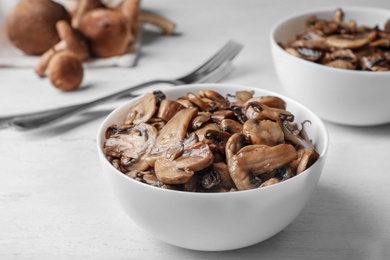 Photo of Bowl with delicious cooked mushrooms on white wooden table