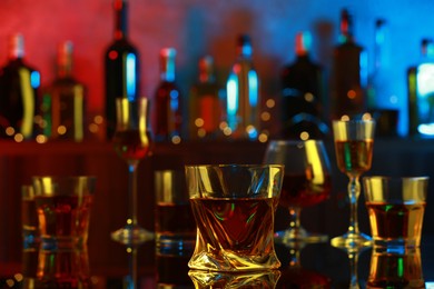 One liqueur in glass in front of others on mirror table in bar