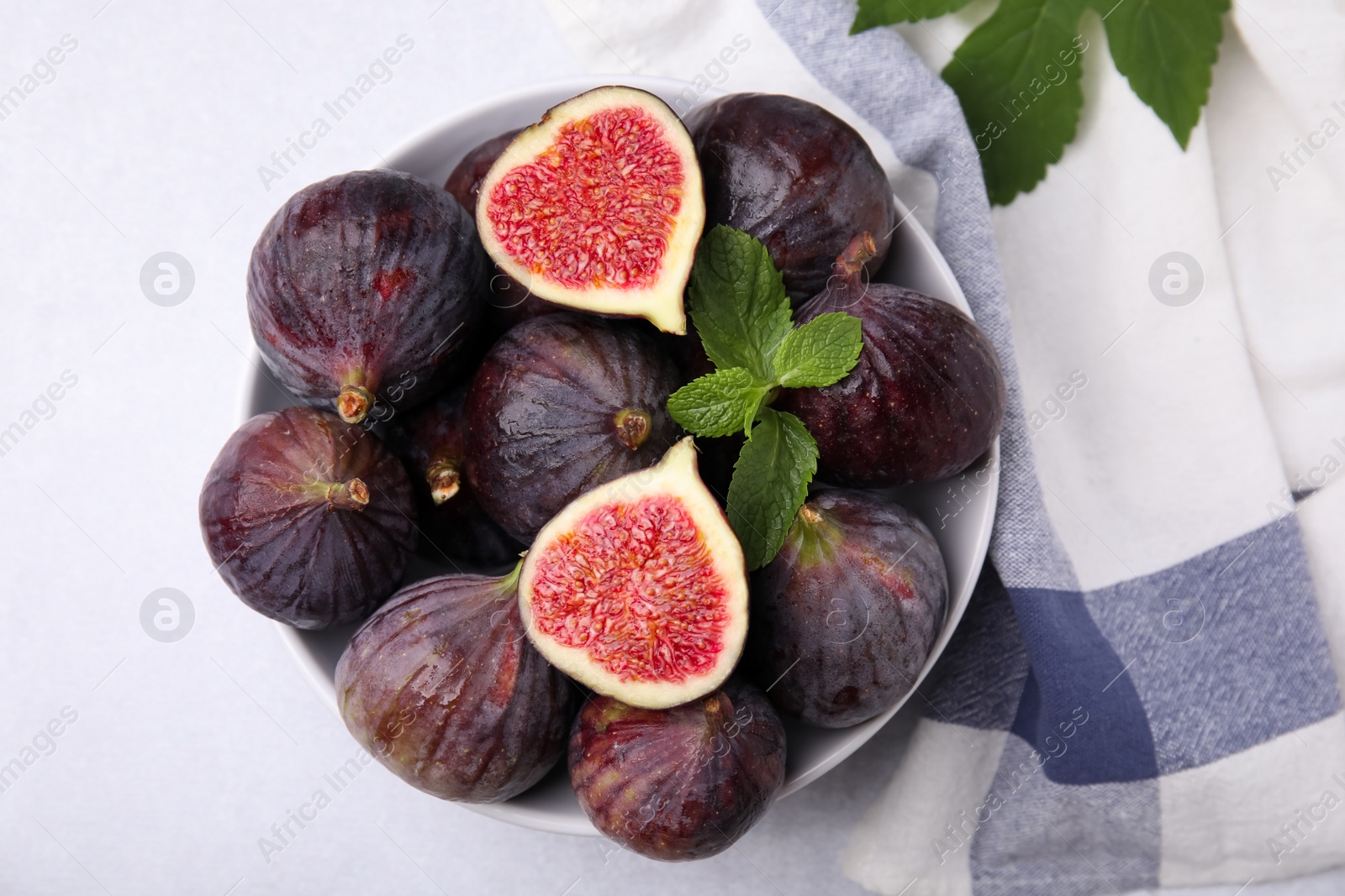 Photo of Bowl of tasty ripe figs on light table, top view