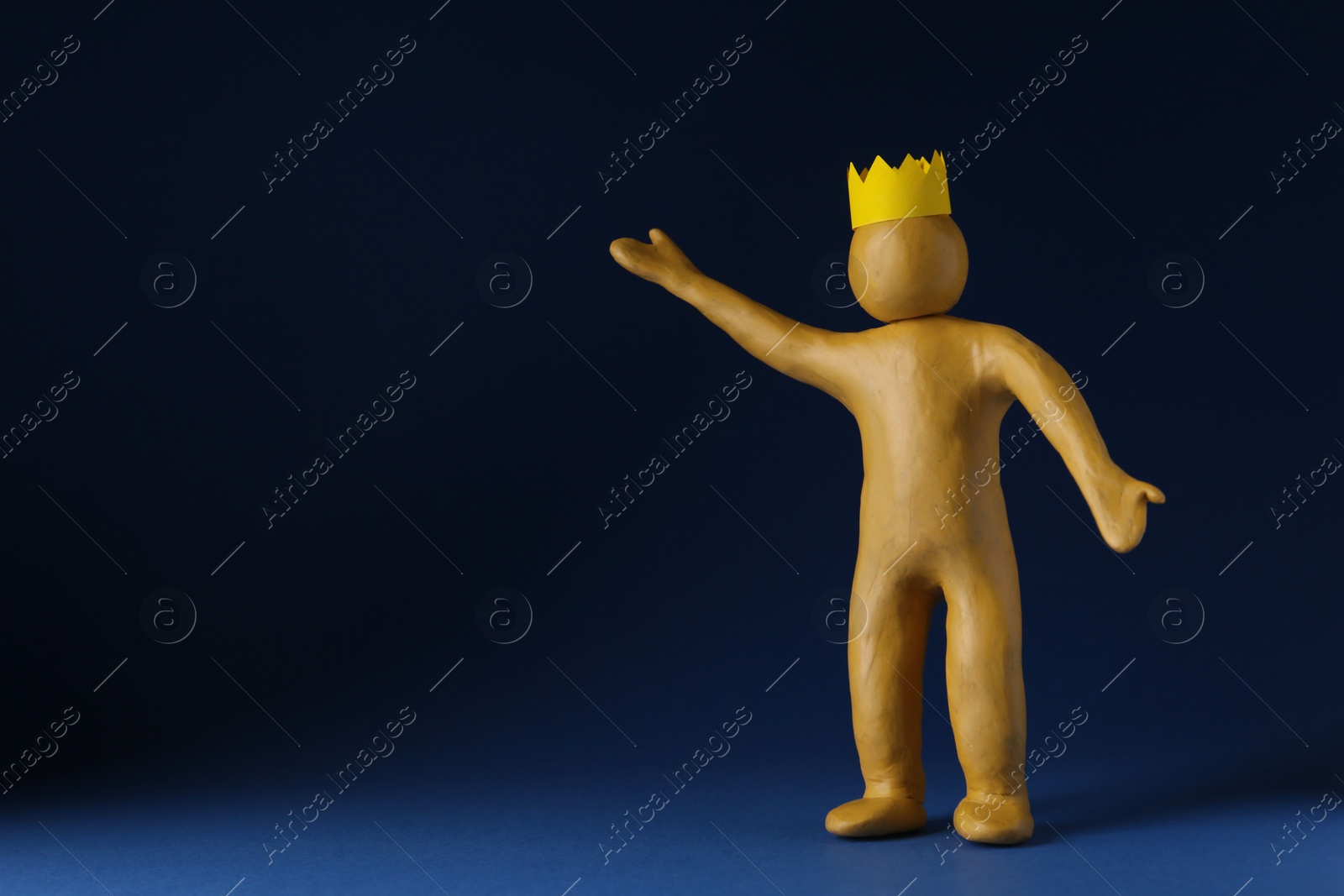 Photo of Plasticine figure with crown on head against dark blue background. Space for text