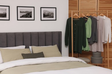 Photo of Comfortable bed and clothes on rack in stylish room