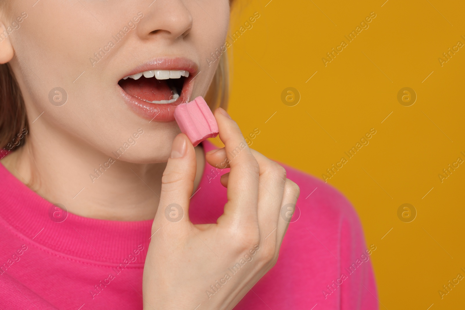 Photo of Woman putting bubble gum into mouth on yellow background, closeup. Space for text