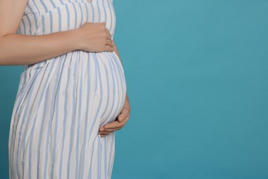 Photo of Pregnant woman on light blue background, closeup. Space for text