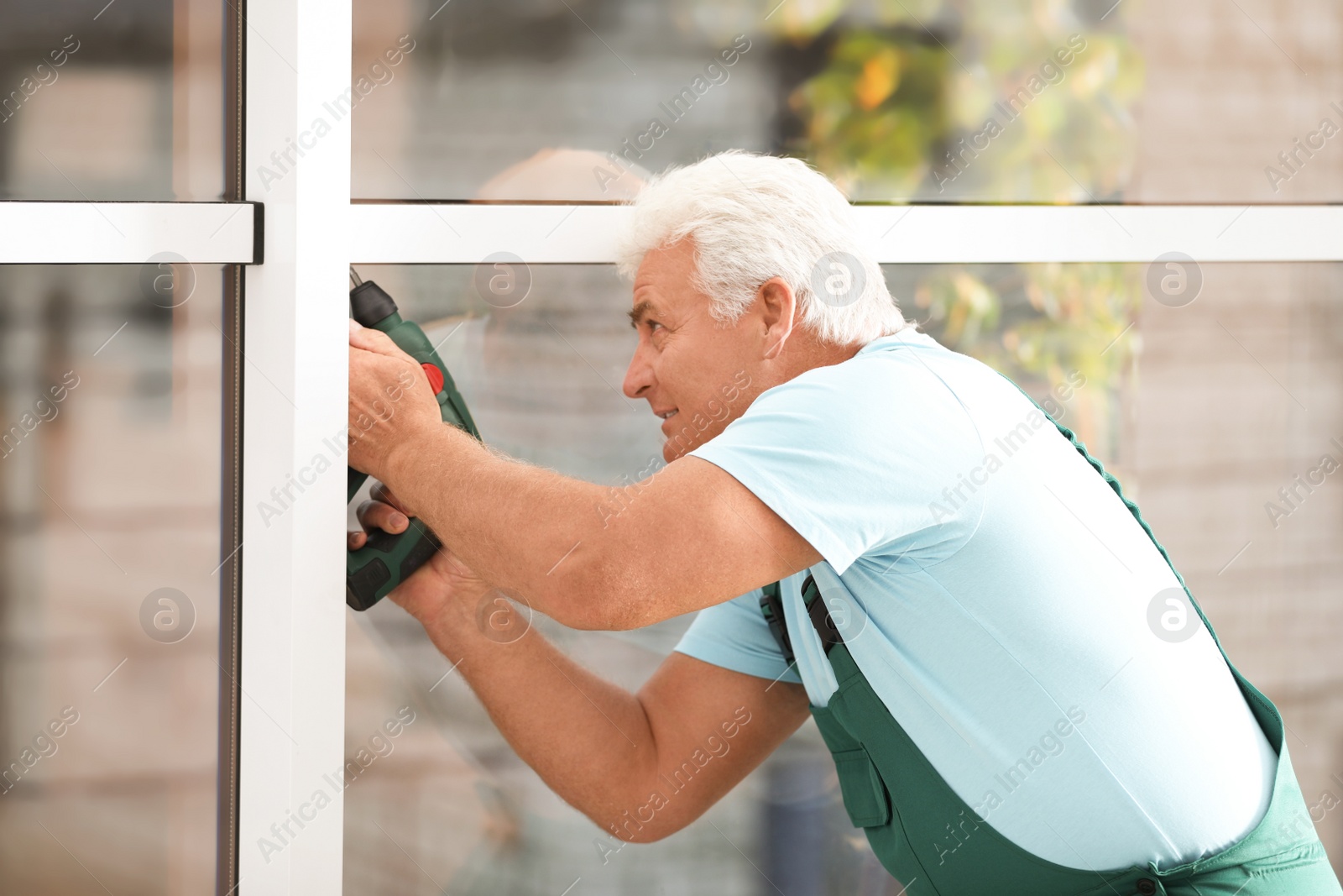 Photo of Mature construction worker repairing plastic window with electric screwdriver indoors