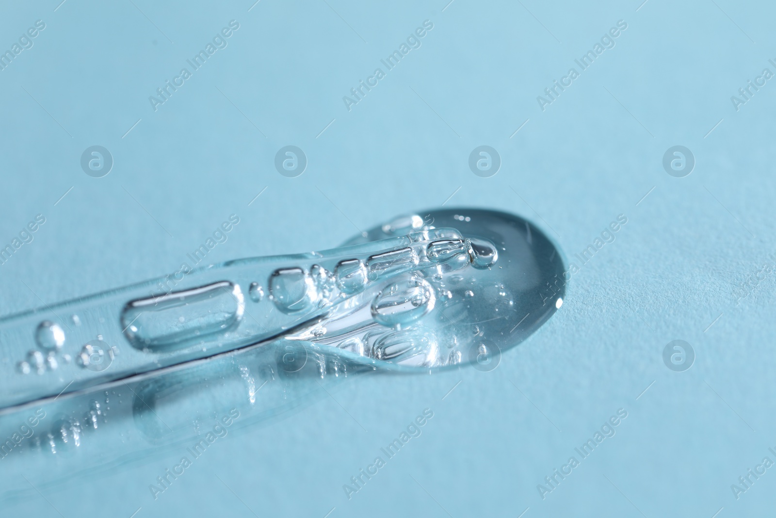 Photo of Glass pipette and transparent liquid on light blue background, closeup