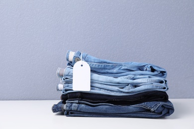 Photo of Stack of stylish jeans with tag on table