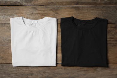 Photo of Stylish white and black T-shirts on wooden table, flat lay
