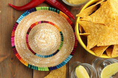 Photo of Mexican sombrero hat, tequila, nachos chips and chili peppers on wooden table, flat lay