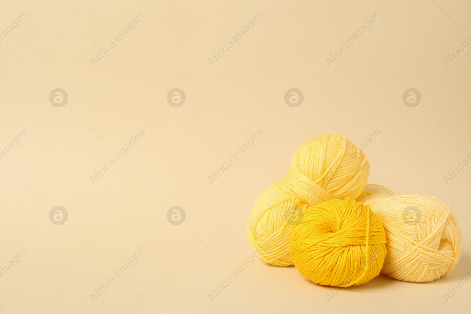 Photo of Soft yellow woolen yarns on beige background, space for text