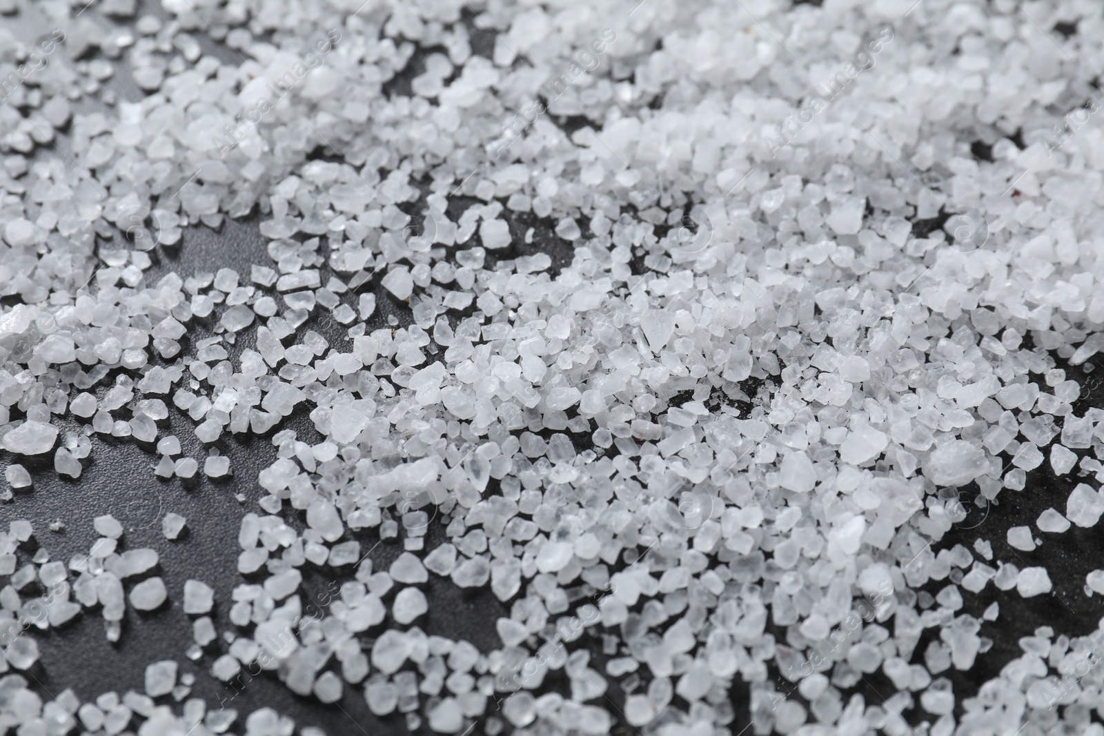 Photo of Scattered natural salt on black table, closeup