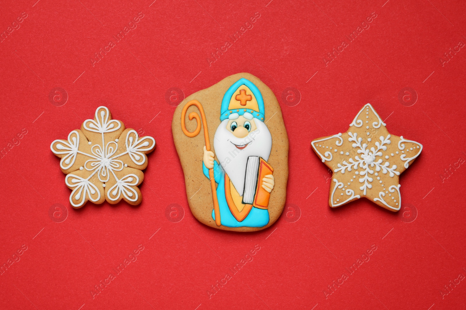 Photo of Tasty gingerbread cookies on red background, flat lay. St. Nicholas Day celebration