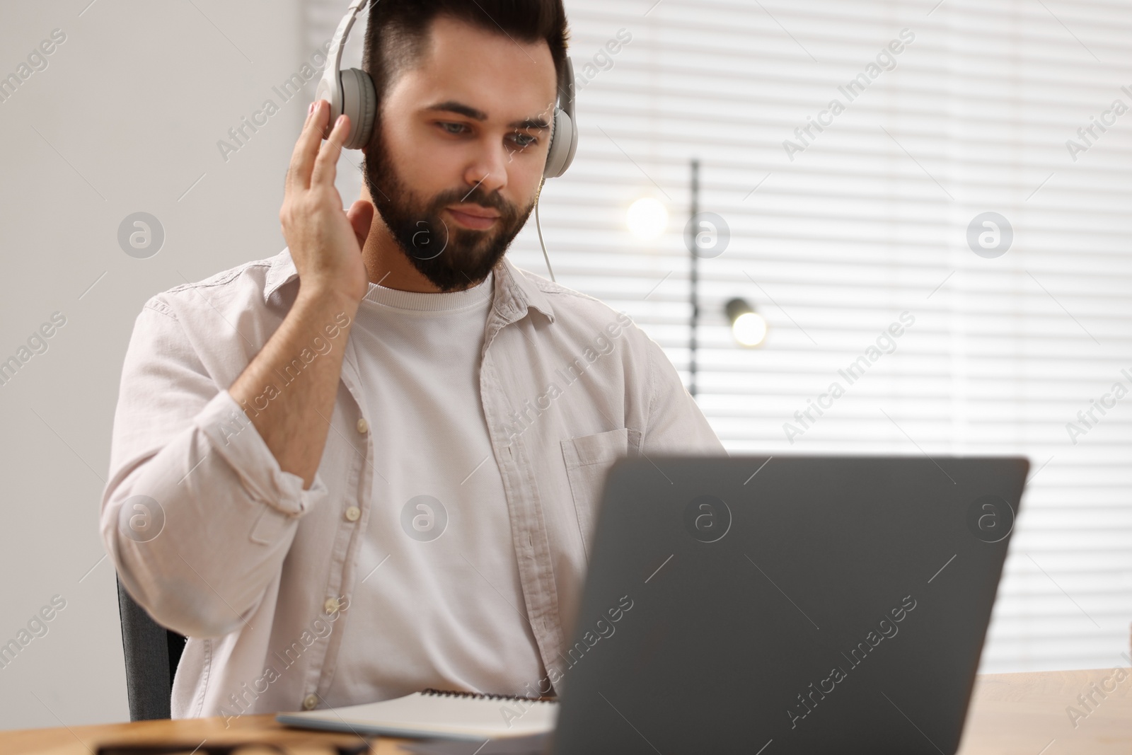 Photo of Young man in headphones watching webinar at table in room