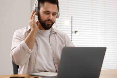 Photo of Young man in headphones watching webinar at table in room