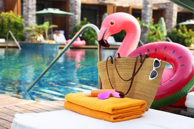 Beach accessories on sun lounger, inflatable ring and float near outdoor swimming pool, space for text. Luxury resort