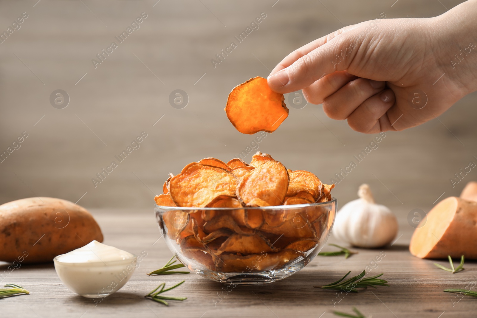 Photo of Woman taking sweet potato chip from bowl on table, closeup